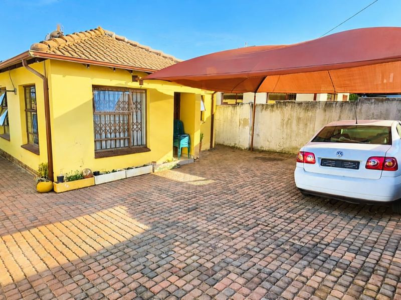 Front exterior view of the house featuring a paved driveway, a shade cloth carport, and secure window bars.