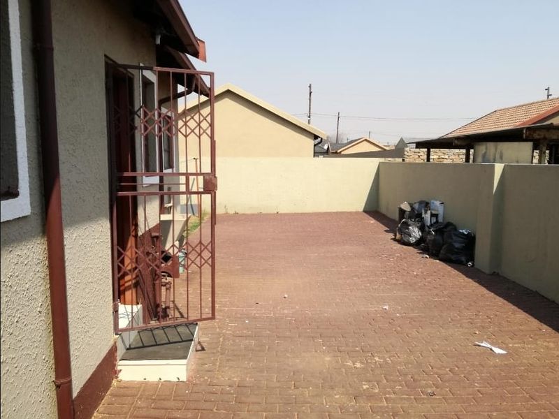 A paved rear courtyard area enclosed by a boundary wall, featuring a security gate access point.