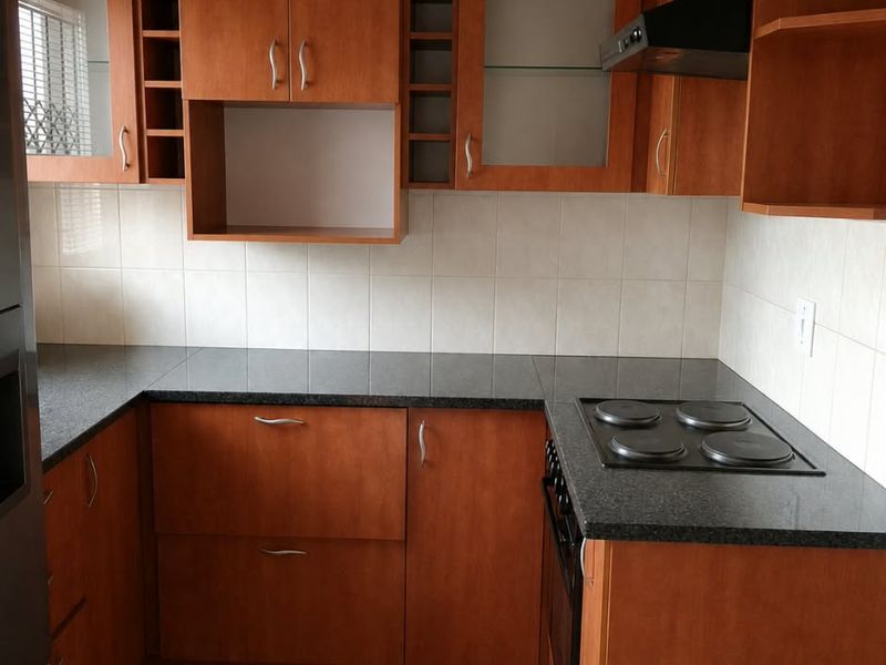 A functional kitchen featuring warm-toned built-in cabinetry, granite countertops, an integrated electric hob and oven, and a tiled backsplash.