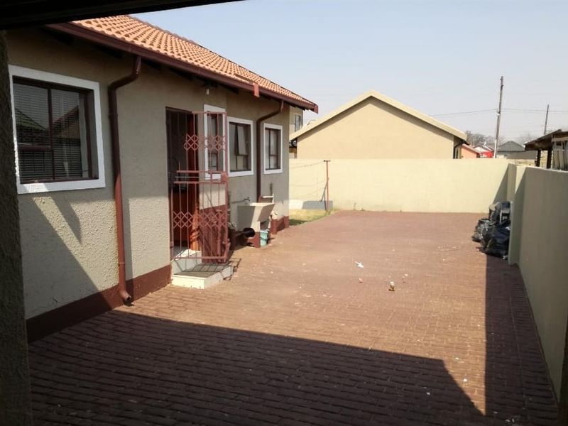 A paved rear courtyard featuring a perimeter wall, security gate, and an external wash basin, offering a functional outdoor space.