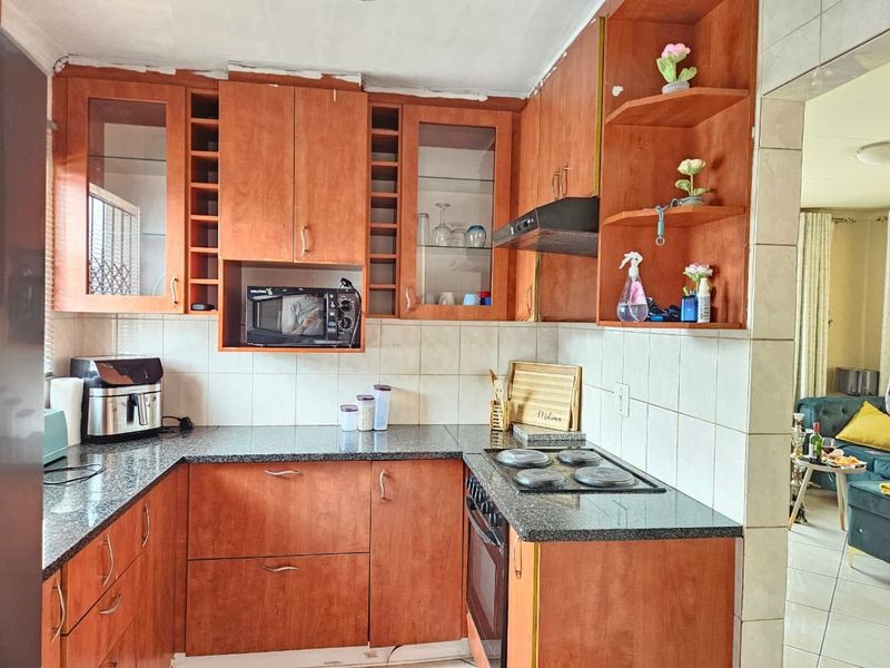 A functional kitchen featuring wooden cabinetry, granite countertops, a built-in oven, and an electric hob with a tiled backsplash.
