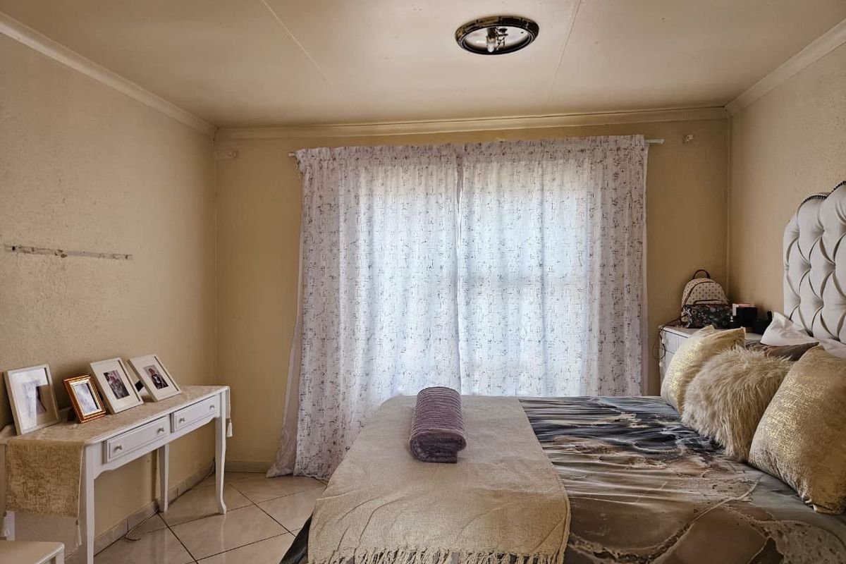 A bedroom featuring tiled flooring and a central ceiling light fixture, with visible wall damage requiring repair.