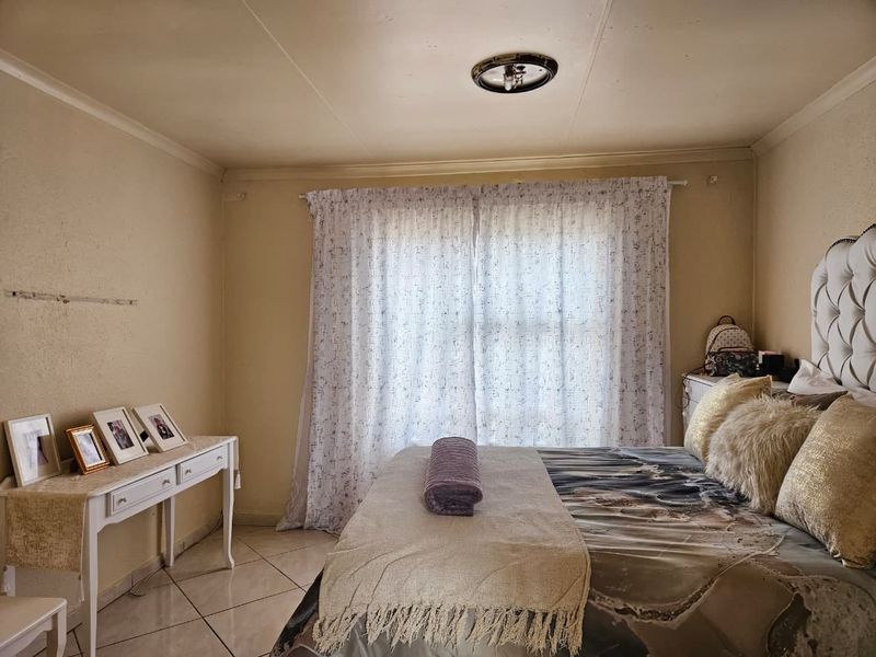 A bedroom featuring tiled flooring and a central ceiling light fixture, with visible wall damage requiring repair.