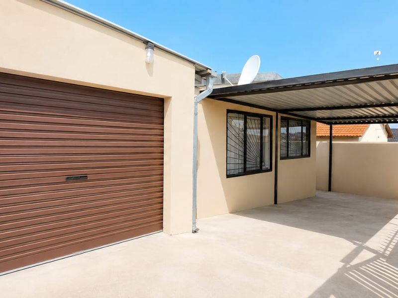 A well-maintained exterior view featuring a single garage with a roller shutter door and an adjacent covered carport area.