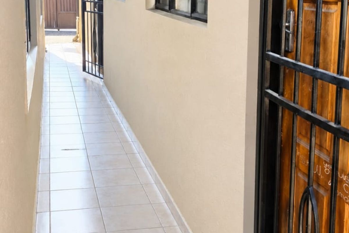 A clean, tiled side walkway or exterior passage featuring a secure metal gate, timber door, and exposed roof rafters.