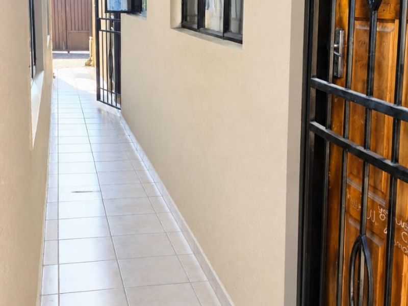 A clean, tiled side walkway or exterior passage featuring a secure metal gate, timber door, and exposed roof rafters.