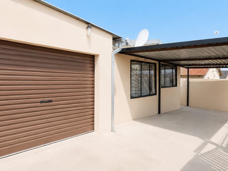A well-maintained garage featuring a brown roller door and an adjacent covered carport area with concrete flooring.
