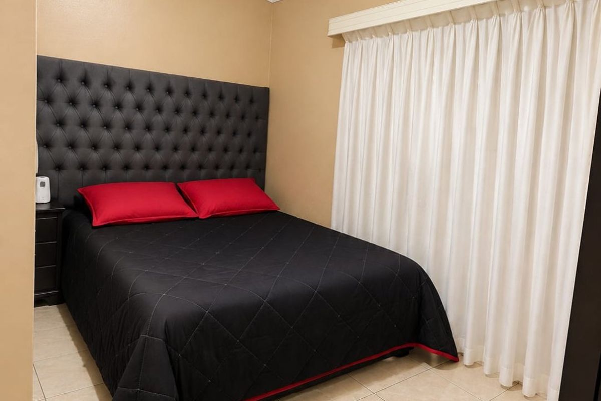 A bedroom featuring tiled flooring, neutral wall paint, and a built-in curtain rail with white curtains.
