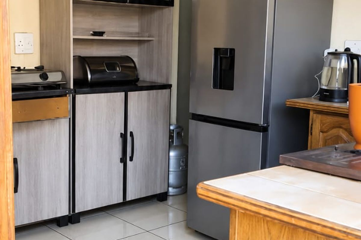 A functional kitchen area featuring tiled flooring and a mix of traditional wooden and modern grey cabinetry with ample storage space.