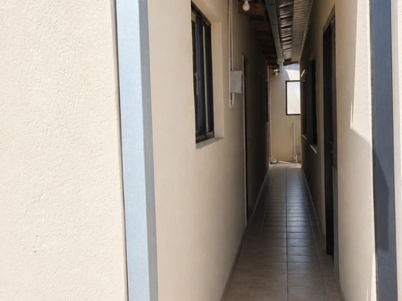 A narrow exterior side passage featuring tiled flooring, exposed timber rafters, and a metal roof covering.