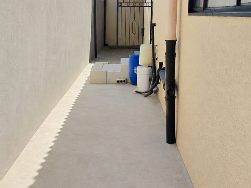 A narrow side passage featuring a concrete pathway, boundary wall, and metal security gate, providing access to the rear of the property.