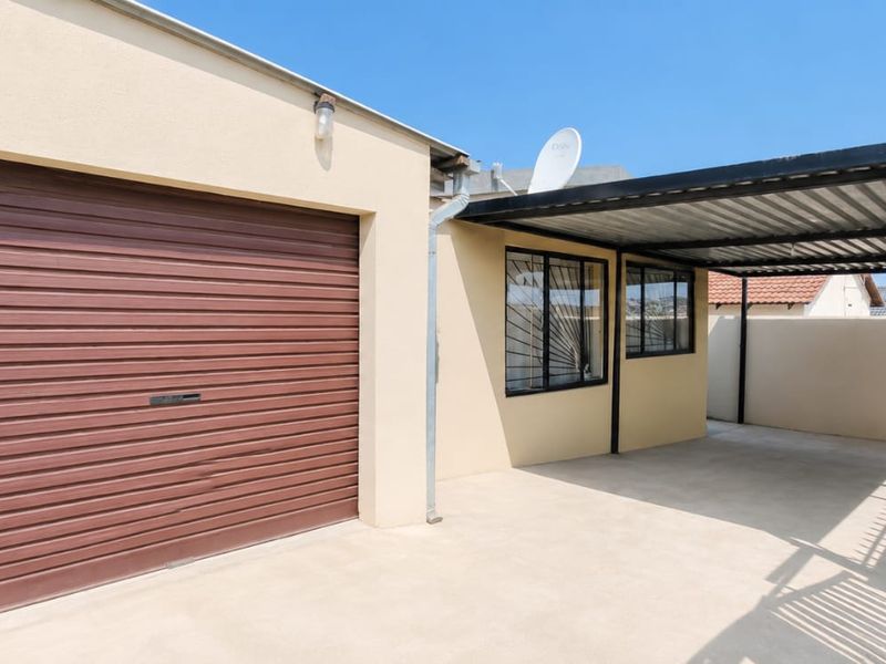 A clean, well-maintained garage area featuring a roller shutter door and an attached carport with concrete flooring.