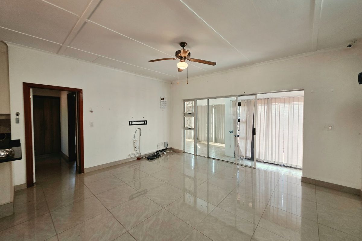 Spacious, empty living area featuring neutral tiled flooring, a ceiling fan, and large sliding glass doors providing access to the exterior.