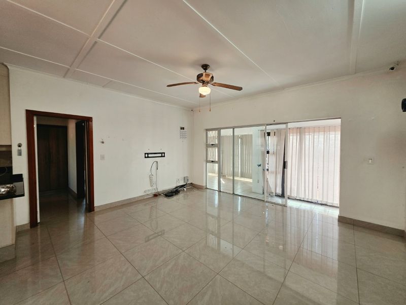 Spacious, empty living area featuring neutral tiled flooring, a ceiling fan, and large sliding glass doors providing access to the exterior.