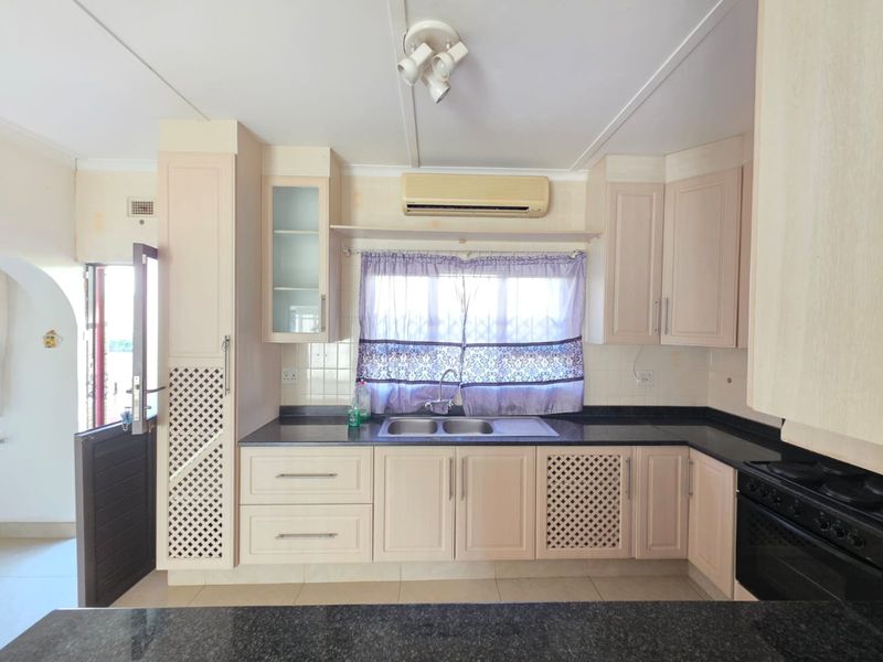 A functional kitchen featuring built-in cabinetry, granite countertops, a double basin sink, and a wall-mounted air conditioning unit.