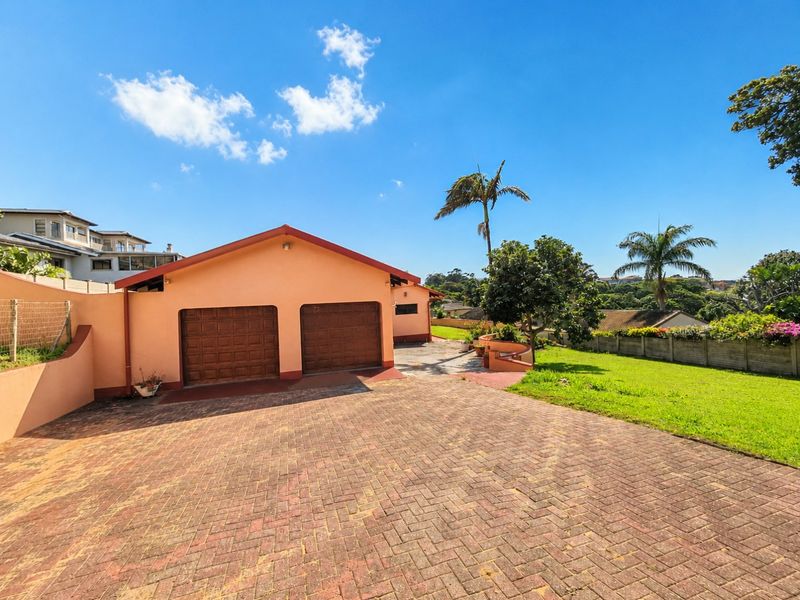 A front exterior view of a residential property featuring a double garage, paved driveway, and landscaped garden area.