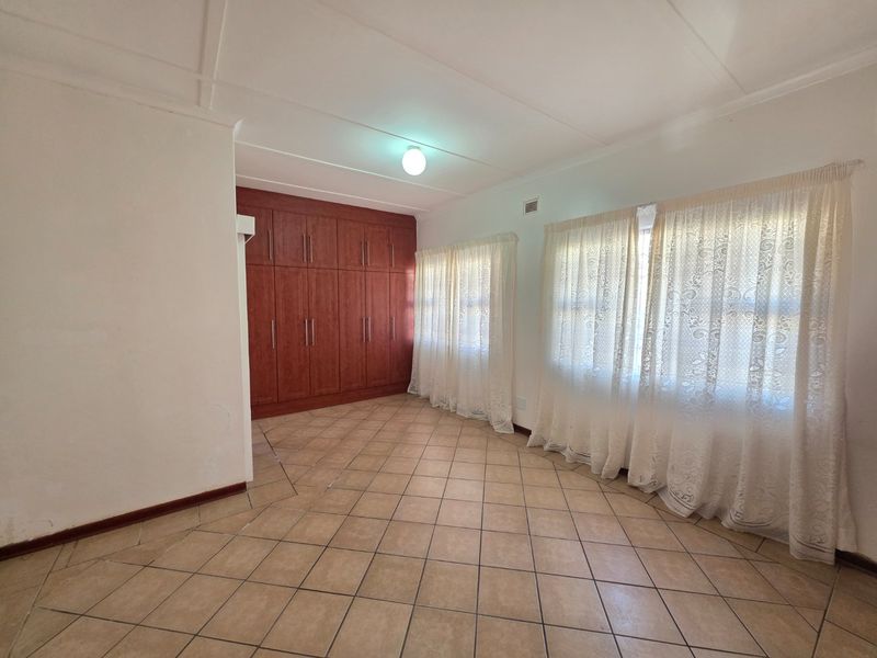 A spacious, empty bedroom featuring neutral tiled flooring and extensive built-in wooden cupboards, offering a clean canvas for personalization.