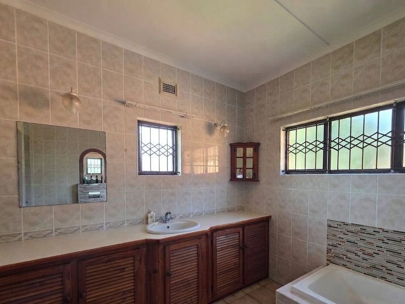 A functional bathroom featuring a built-in vanity with basin, tiled walls, and a bathtub, offering a classic layout with potential for modern updates.
