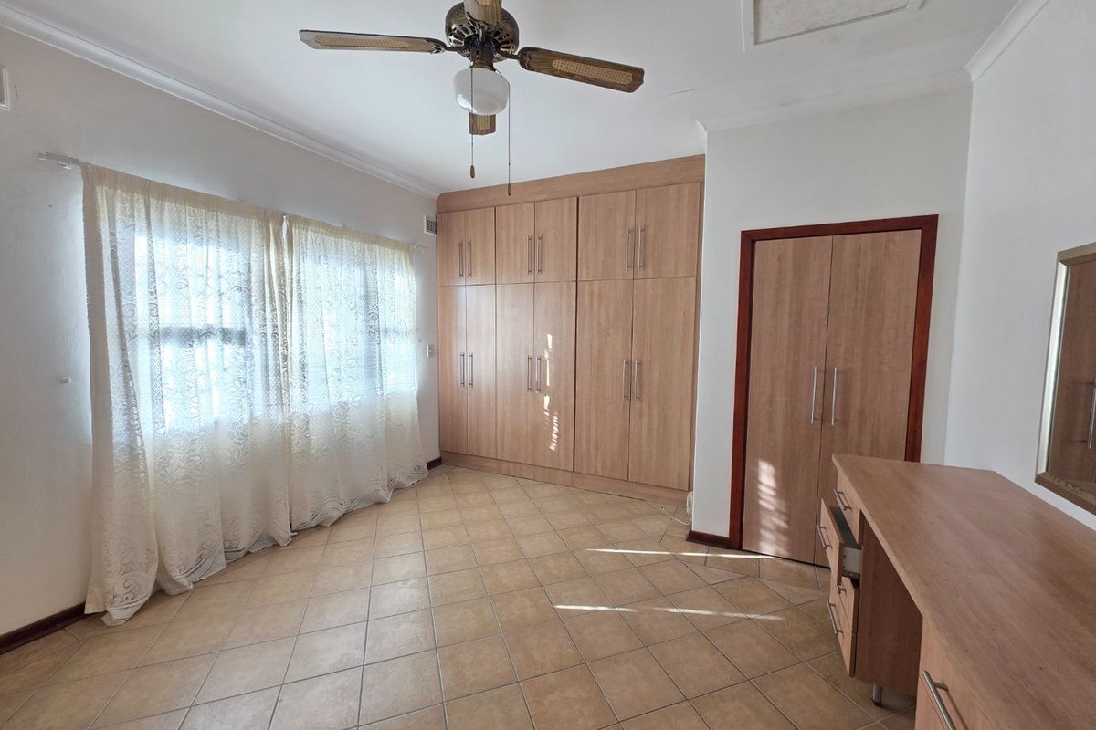 A bedroom featuring tiled flooring, extensive built-in wooden cabinetry, a ceiling fan, and a built-in vanity unit.