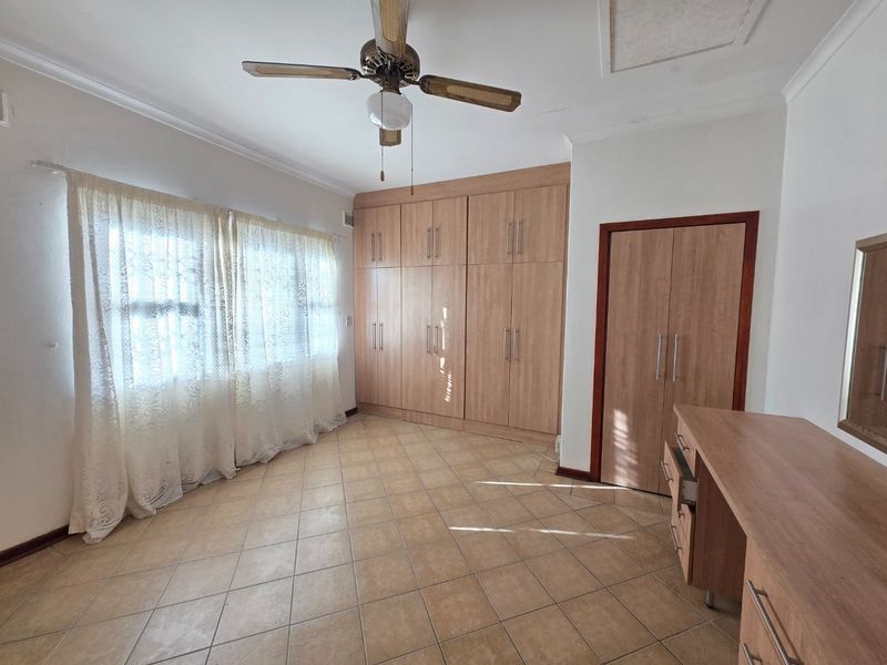 A bedroom featuring tiled flooring, extensive built-in wooden cabinetry, a ceiling fan, and a built-in vanity unit.