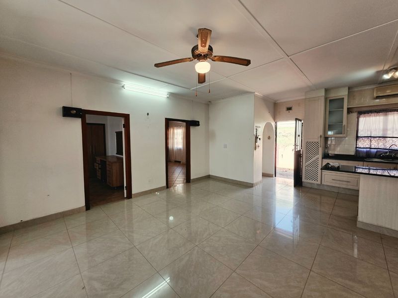 Spacious open-plan living area featuring tiled flooring, a ceiling fan, and an integrated kitchen with granite countertops and built-in cabinetry.