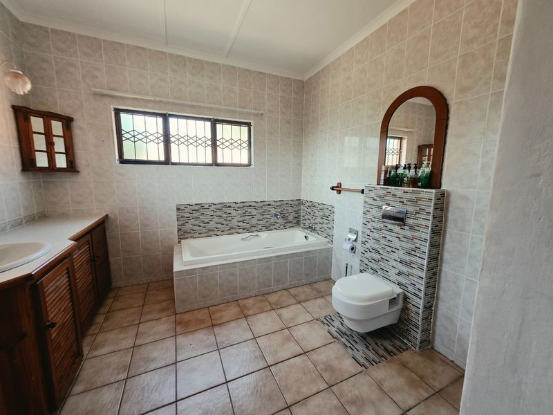 Spacious bathroom featuring a built-in vanity, drop-in bathtub, and wall-mounted toilet with neutral tiled finishes throughout.