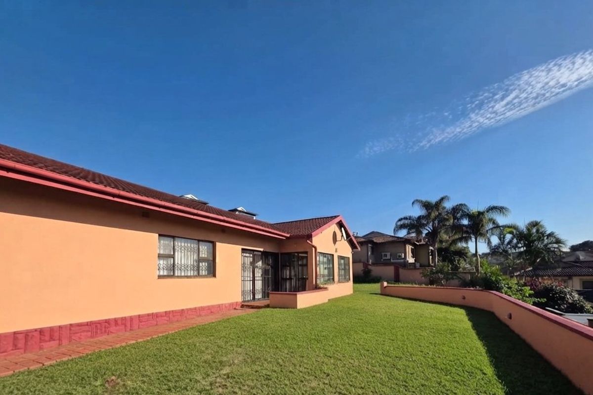 Rear view of the house featuring a well-maintained lawn, paved walkway, and a retaining wall, showcasing the property's exterior structure and garden space.