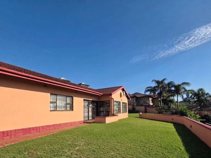 Rear view of the house featuring a well-maintained lawn, paved walkway, and a retaining wall, showcasing the property's exterior structure and garden space.