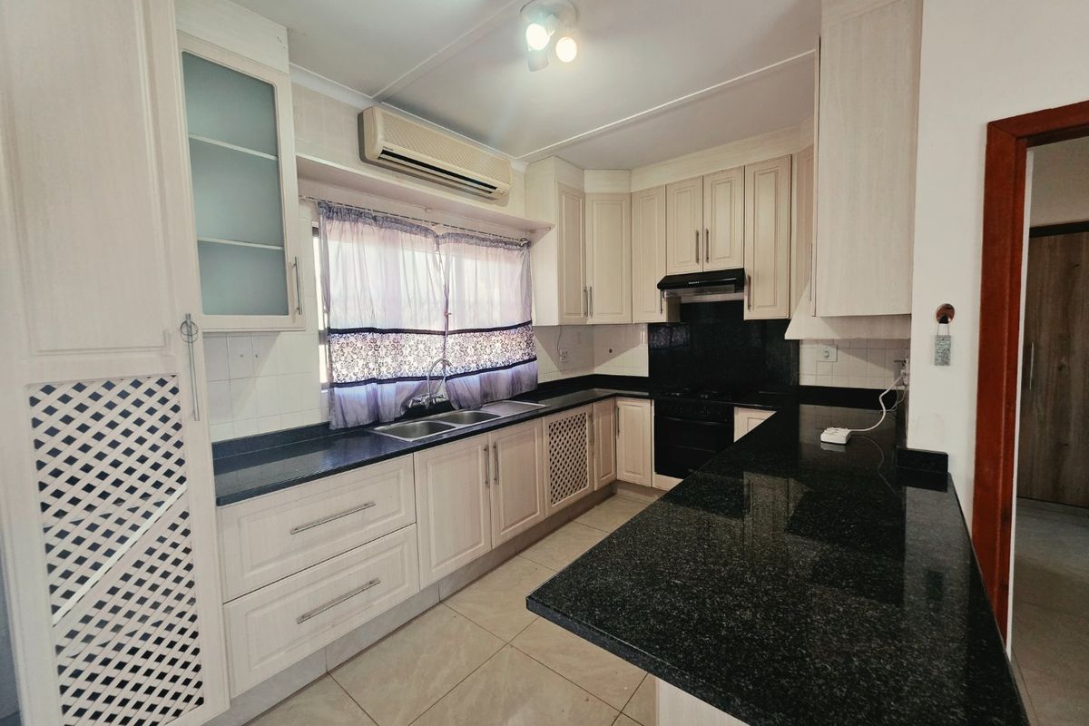 A functional kitchen featuring light-toned cabinetry, dark granite countertops, a double basin sink, and built-in cooking appliances with tiled flooring.