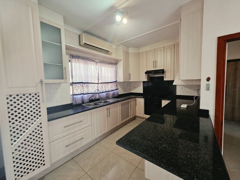 A functional kitchen featuring light-toned cabinetry, dark granite countertops, a double basin sink, and built-in cooking appliances with tiled flooring.