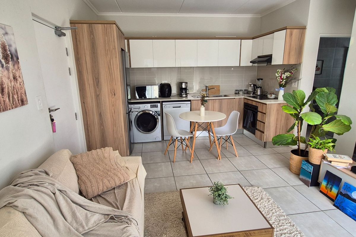 Modern open-plan living area featuring a well-appointed kitchen with built-in cabinetry, integrated appliances, and neutral tiled flooring throughout.
