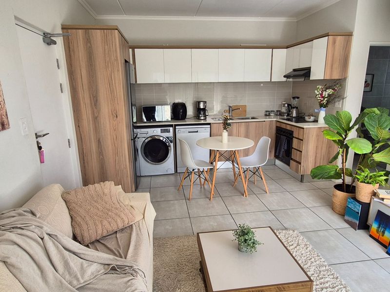 Modern open-plan living area featuring a well-appointed kitchen with built-in cabinetry, integrated appliances, and neutral tiled flooring throughout.