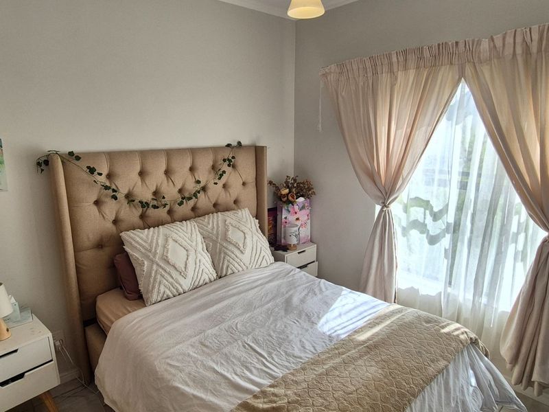 A cozy bedroom featuring neutral wall tones, natural light through a window with curtains, and standard electrical fixtures.