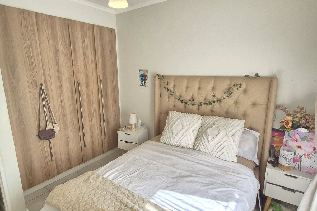 A well-maintained bedroom featuring modern wood-finish built-in cupboards and neutral tiled flooring, with an adjoining view into the bathroom.
