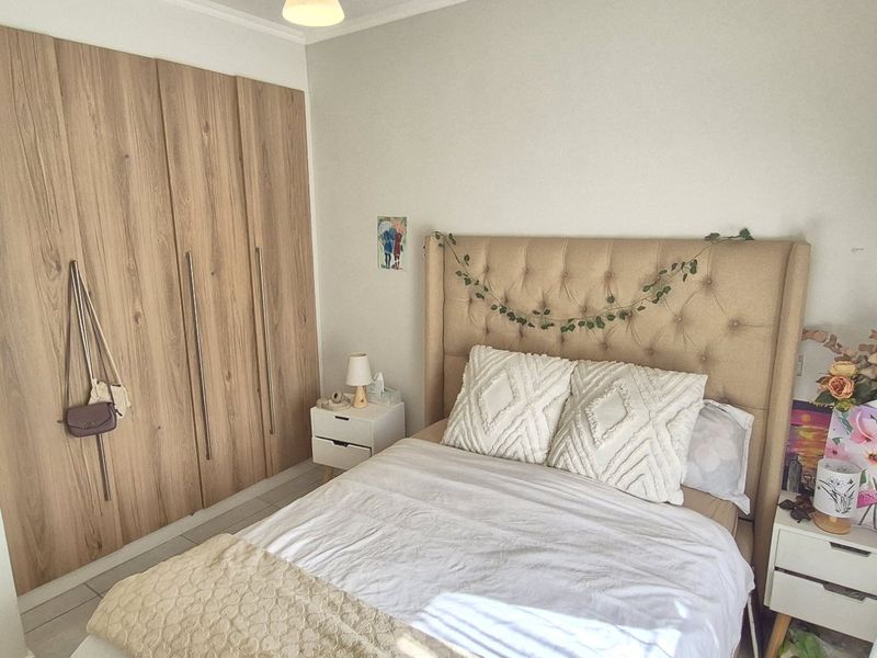 A well-maintained bedroom featuring modern wood-finish built-in cupboards and neutral tiled flooring, with an adjoining view into the bathroom.