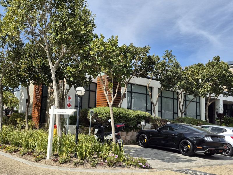 Front exterior view of the apartment complex featuring landscaped gardens, paved driveway, and modern architectural elements with large glass windows.