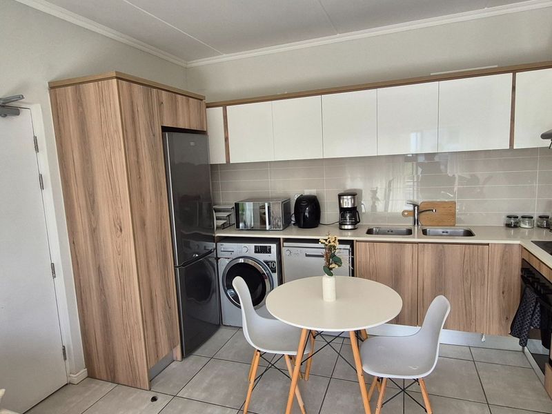 Modern open-plan kitchen featuring wood-grain and white cabinetry, integrated appliances, tiled backsplash, and neutral floor tiles in a well-maintained apartment setting.