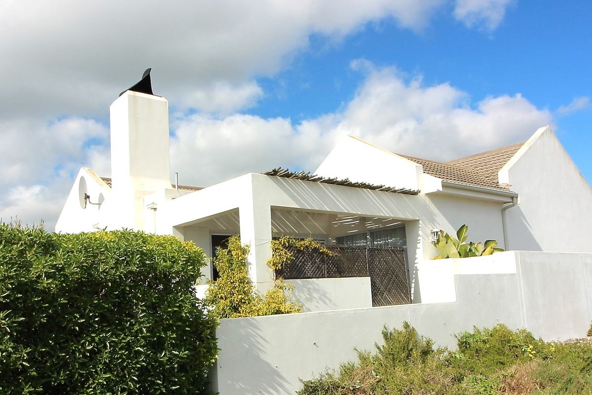 Rear view of the property featuring a covered patio area with a pergola, a prominent chimney, and a surrounding boundary wall.