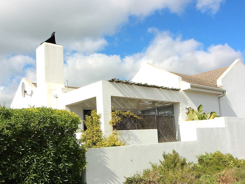 Rear view of the property featuring a covered patio area with a pergola, a prominent chimney, and a surrounding boundary wall.