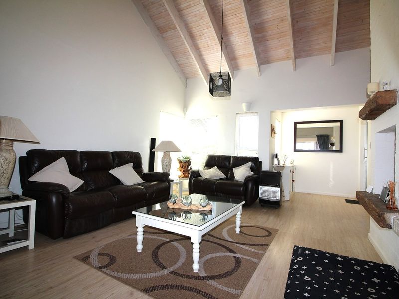 Spacious living room featuring a high vaulted timber ceiling with exposed beams, laminate flooring, and a characterful brick fireplace with a timber mantel.
