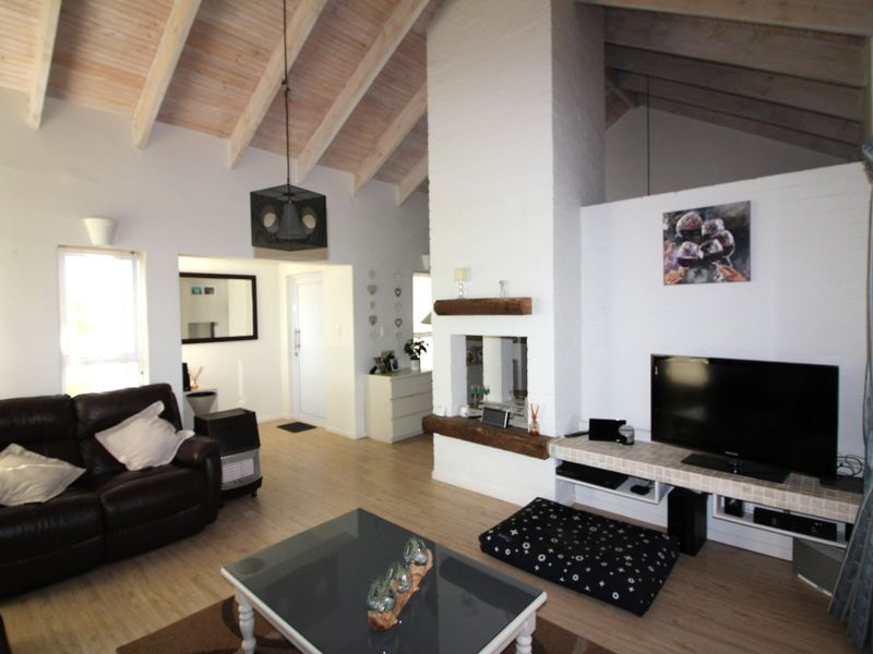 Spacious living room featuring a vaulted timber ceiling, a central exposed brick fireplace with a timber mantel, and light-toned laminate flooring.
