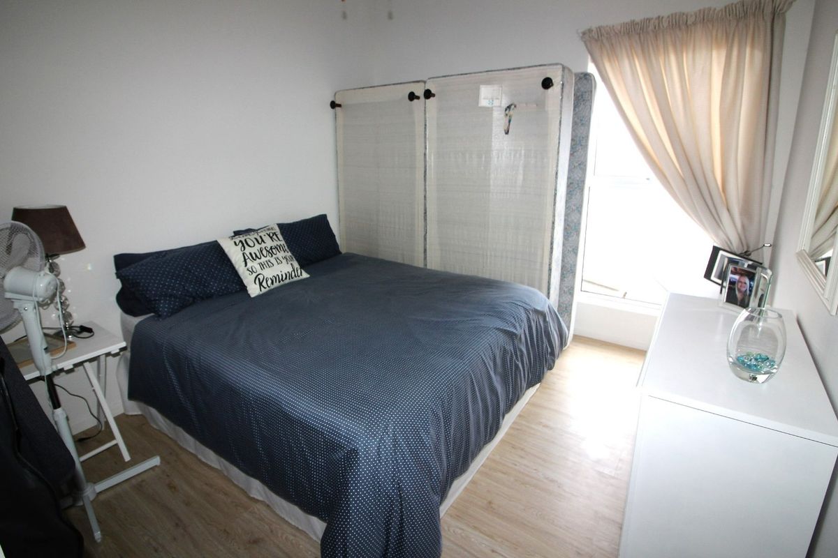 A functional bedroom featuring light-toned laminate flooring and a window with installed curtain rails, providing a neutral base for interior design.