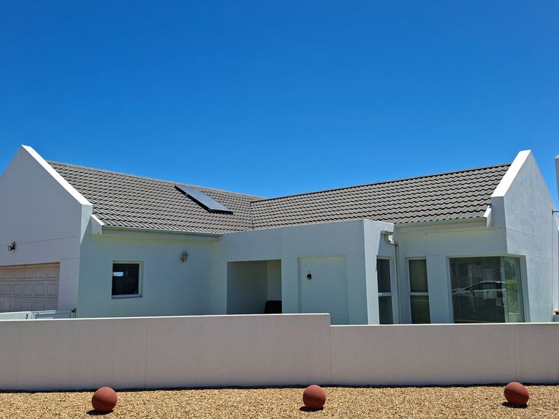 Front elevation of a modern white house featuring a tiled roof, solar panel, chimney, and a secure boundary wall.