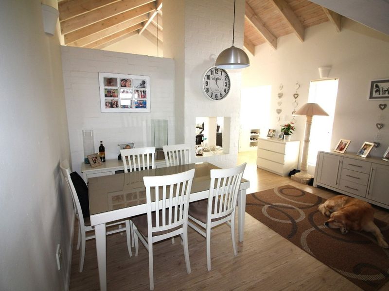 Dining area featuring a vaulted ceiling with exposed timber rafters, laminate flooring, and a central brick fireplace.