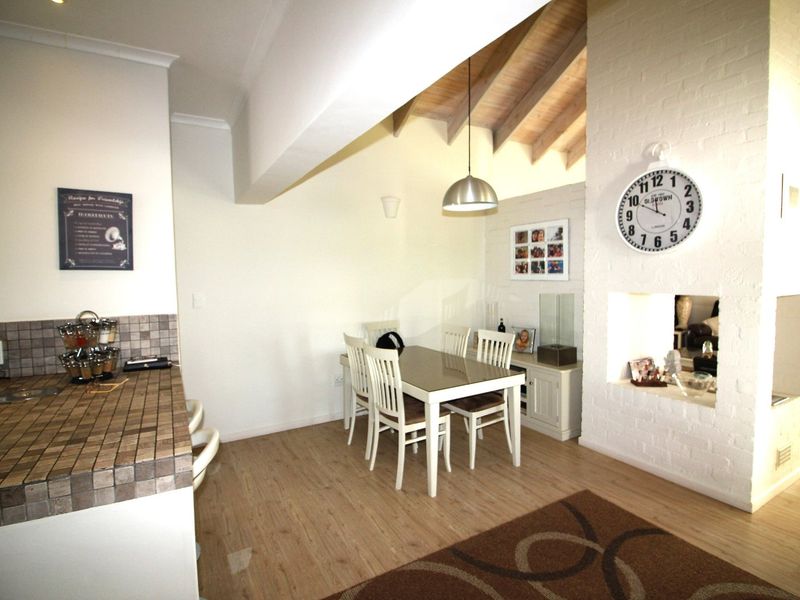 Open-plan living and dining area featuring vaulted ceilings with exposed timber rafters, a brick fireplace, and a tiled kitchen counter.