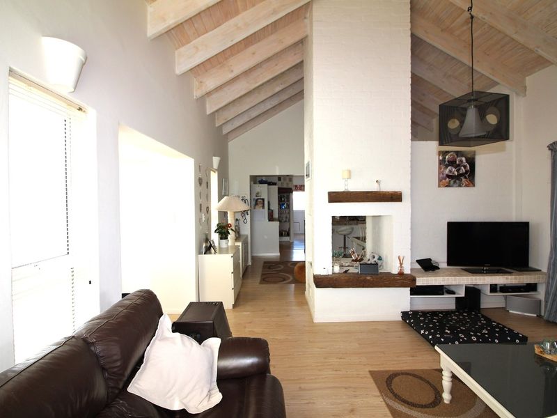 Spacious living room featuring a vaulted ceiling with exposed timber rafters, a central brick fireplace with a timber mantel, and light laminate flooring.