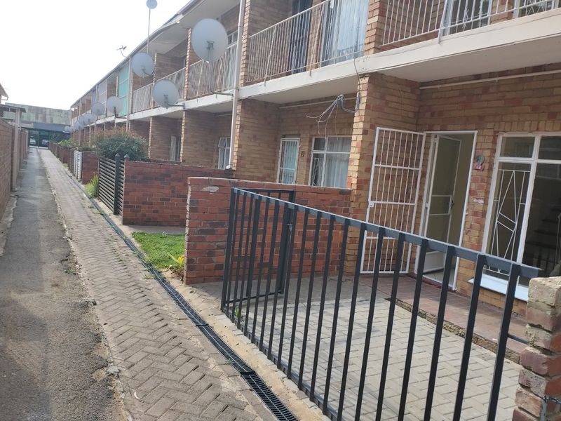 Exterior view of a multi-unit townhouse complex featuring brick facades, metal security gates, and a paved communal walkway.
