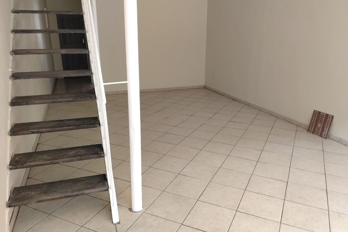 An empty living area featuring tiled flooring and an open staircase with a central support column.