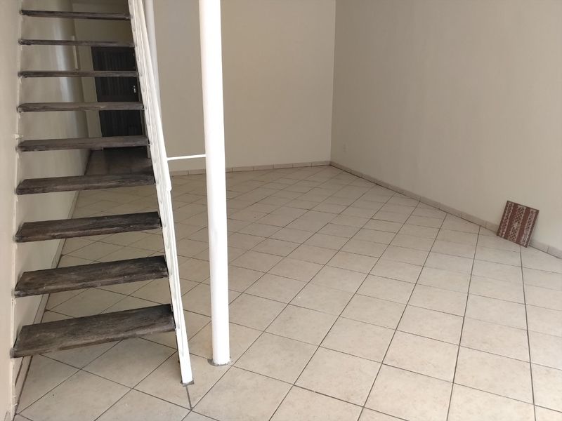 An empty living area featuring tiled flooring and an open staircase with a central support column.
