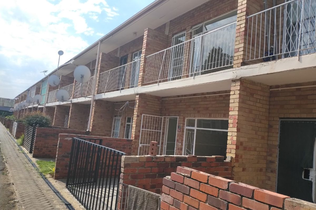 Rear view of a multi-story townhouse complex featuring face brick construction, private balcony access, and individual ground-level courtyard spaces.